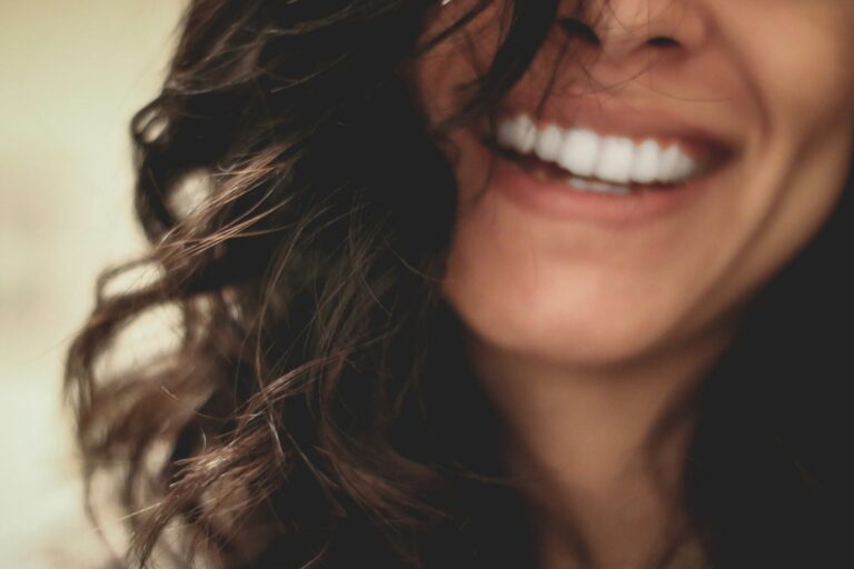 Close-up of a smiling person with dark curly hair and bright white teeth