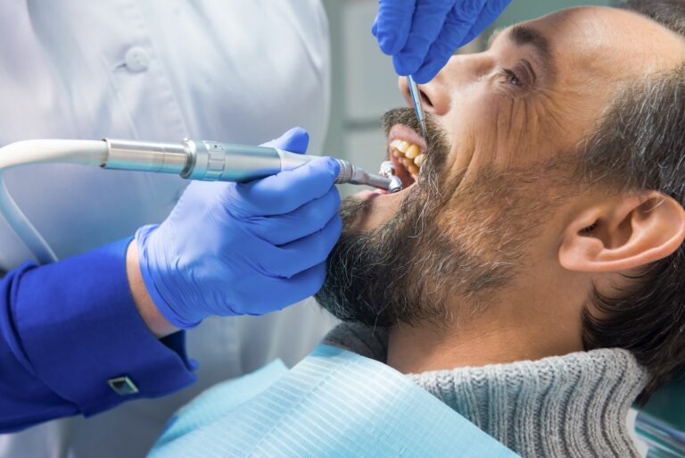Dentist using a drill while examining a patient’s teeth in a dental chair