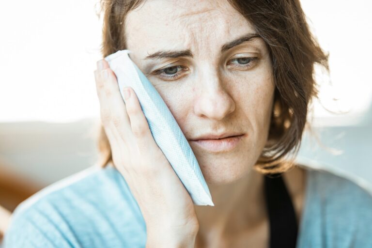 Woman holding a cold compress to her cheek with a pained expression