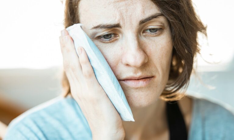 Woman holding a cold compress to her cheek with a pained expression