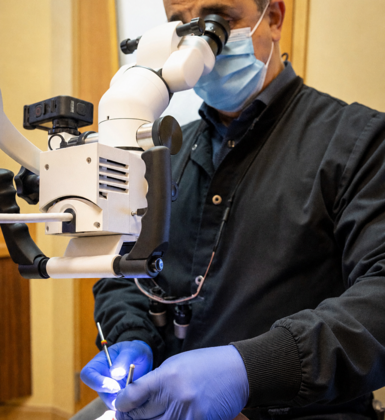 Masked dental clinician uses a microscope and instruments during a close-up procedure