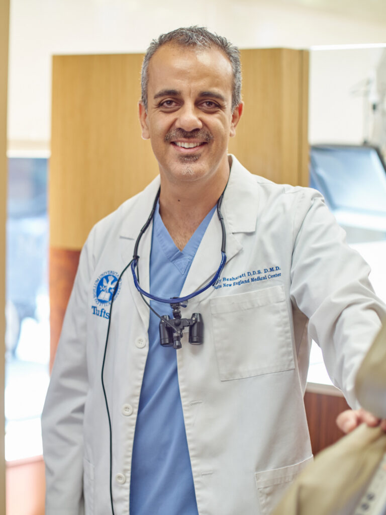 Dr. Ray Besharati, DMD, wearing surgical loupes and a Tufts lab coat in a dental operatory