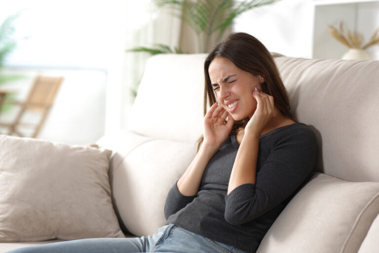 Woman on a couch wincing and holding her ears in discomfort