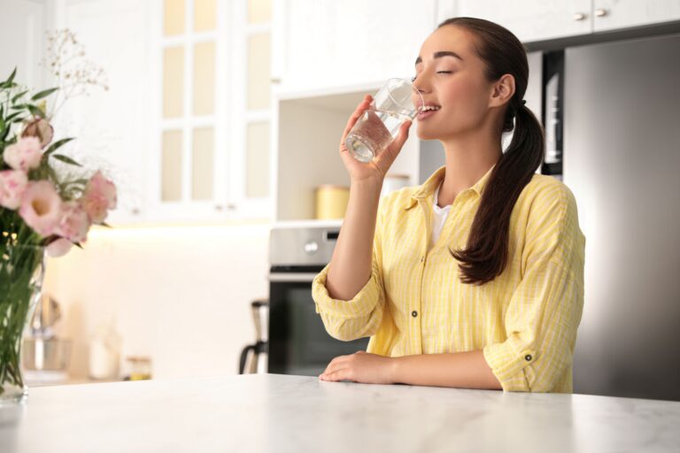 Woman drinking a glass of water in a bright kitchen