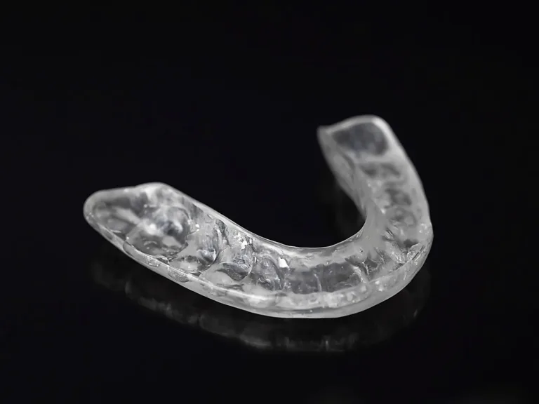 Clear hard dental night guard on a glossy black surface.