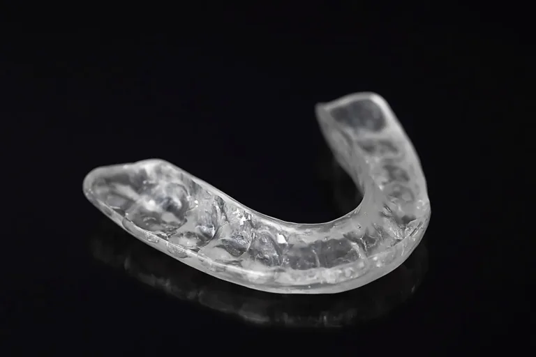 Clear hard dental night guard on a glossy black surface.