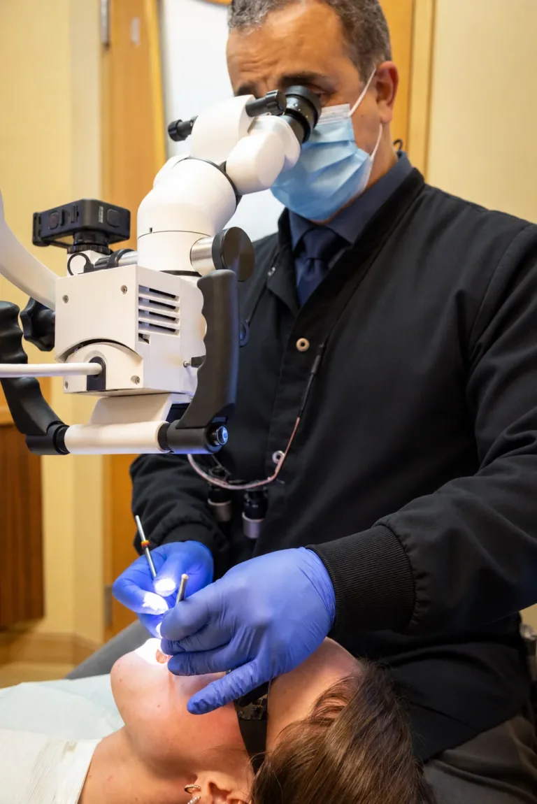 Masked dental clinician uses a microscope and instruments during a close-up procedure